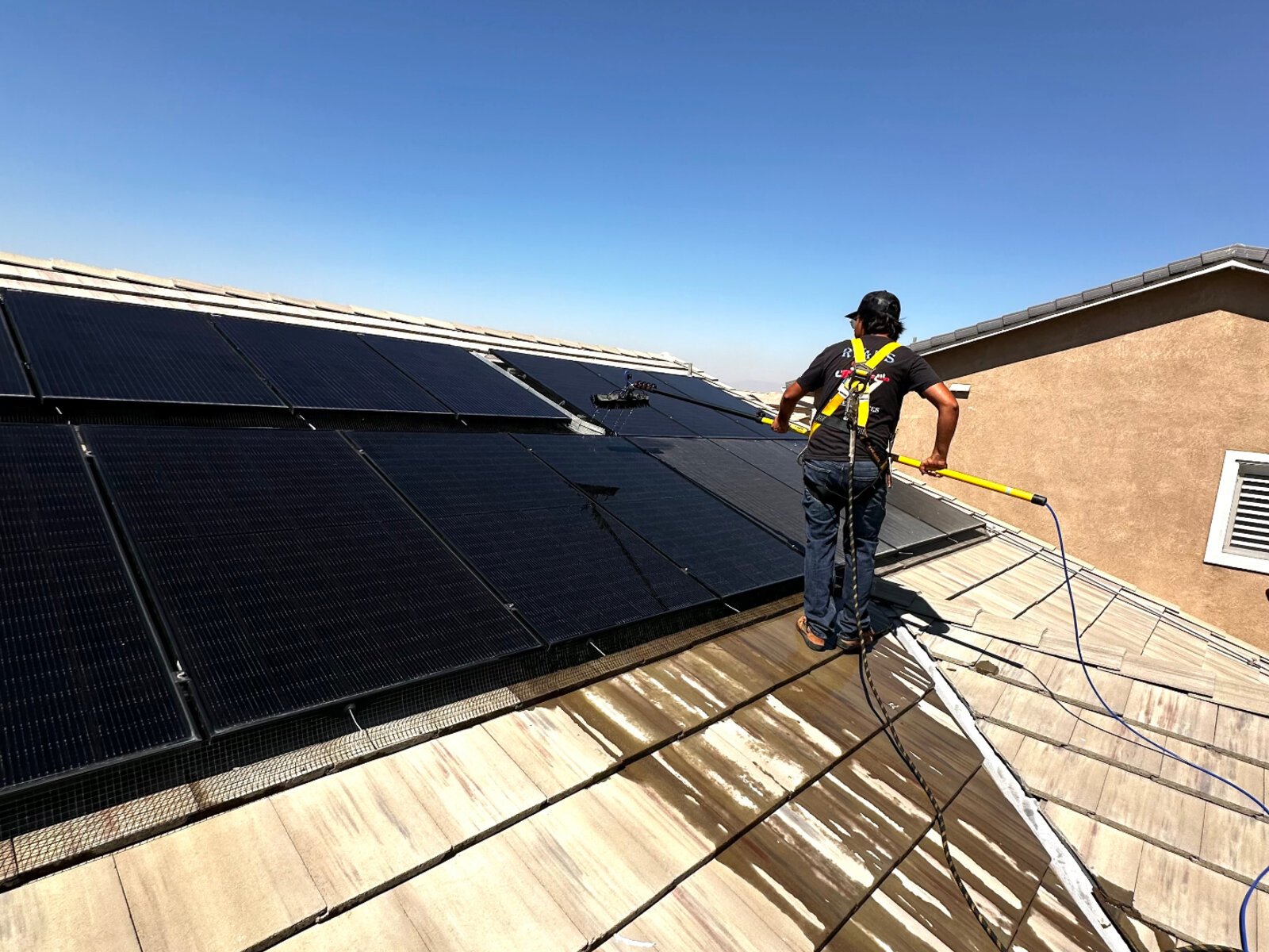 Technician cleaning rooftop solar panels with extension brush in Inland Empire